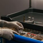 Mãos enluvadas organizam frascos de medicamento em um ambiente clínico.