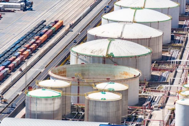 Vista aérea de grandes tanques de armazenamento de combustíveis em área industrial, junto a trilhos ferroviários.