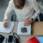 Homem analisa documentos financeiros com uma calculadora sobre a mesa em um escritório.