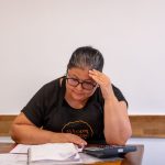 Empreendedora analisa anotações e faz cálculos financeiros em uma mesa de trabalho.