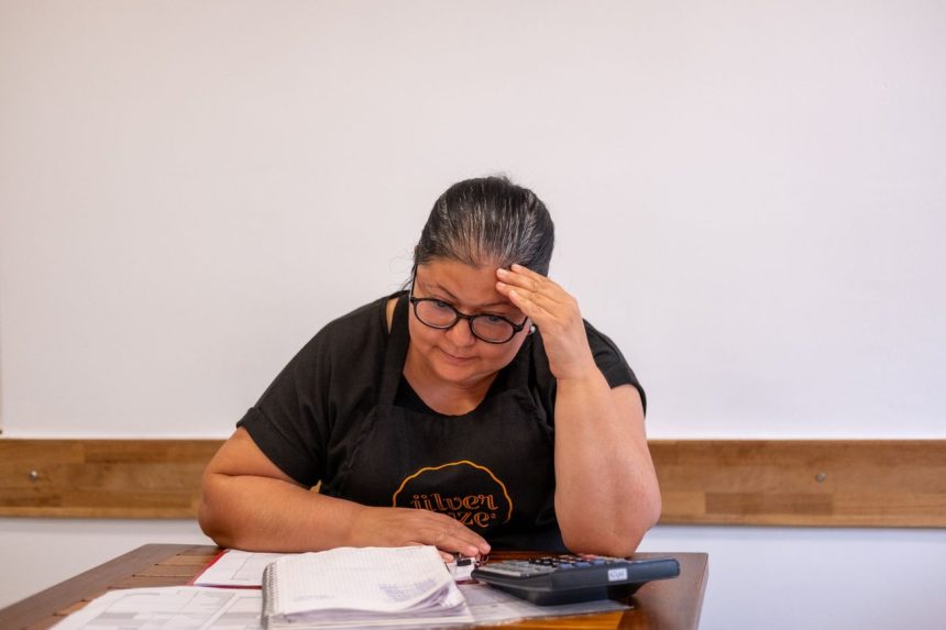 Empreendedora analisa anotações e faz cálculos financeiros em uma mesa de trabalho.