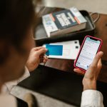 Pessoa realiza um pagamento digital pelo celular enquanto segura um cartão, em ambiente interno.