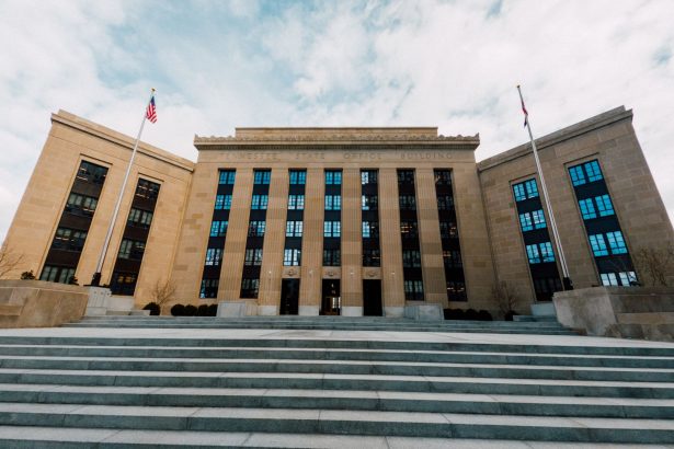 Vista externa do edifício do Federal Reserve, com bandeiras dos Estados Unidos e escadaria sob céu nublado.