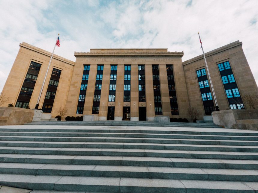 Vista externa do edifício do Federal Reserve, com bandeiras dos Estados Unidos e escadaria sob céu nublado.